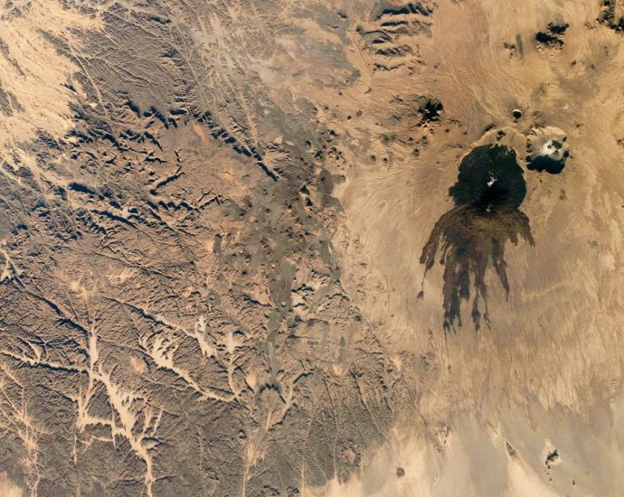 Shadowy tendrils of ancient lava have scarred a dark volcano next to a ‘skull’ in the Sahara — Earth from space